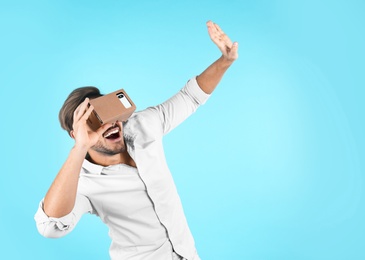 Young man using cardboard virtual reality headset on color background. Space for text