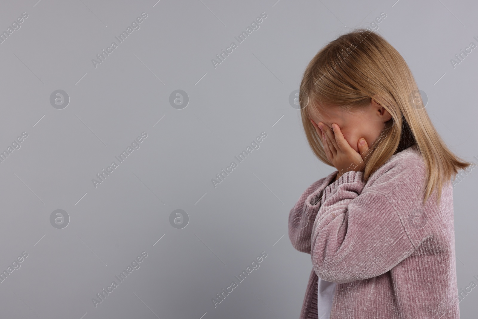 Photo of Resentful girl covering face with hands on grey background. Space for text