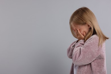 Photo of Resentful girl covering face with hands on grey background. Space for text