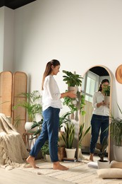 Photo of Young woman decorating room with houseplants at home