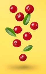 Delicious ripe cranberries and fresh leaves falling on yellow background