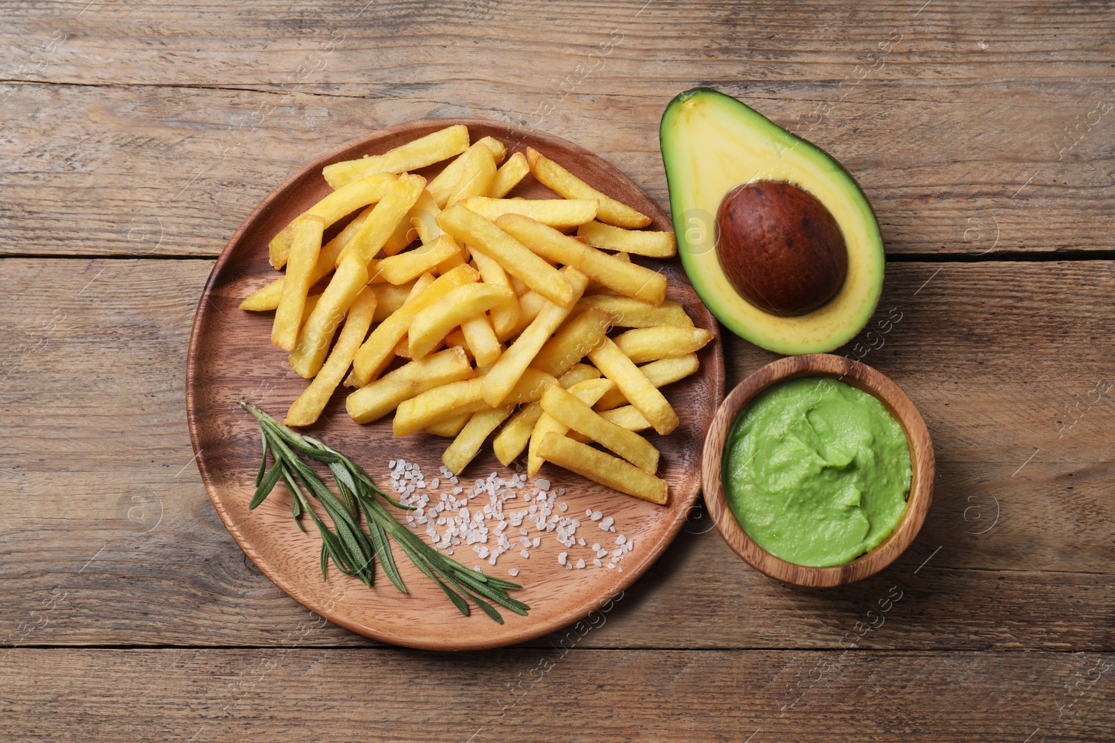 Photo of Plate with french fries, guacamole dip and avocado served on wooden table, flat lay