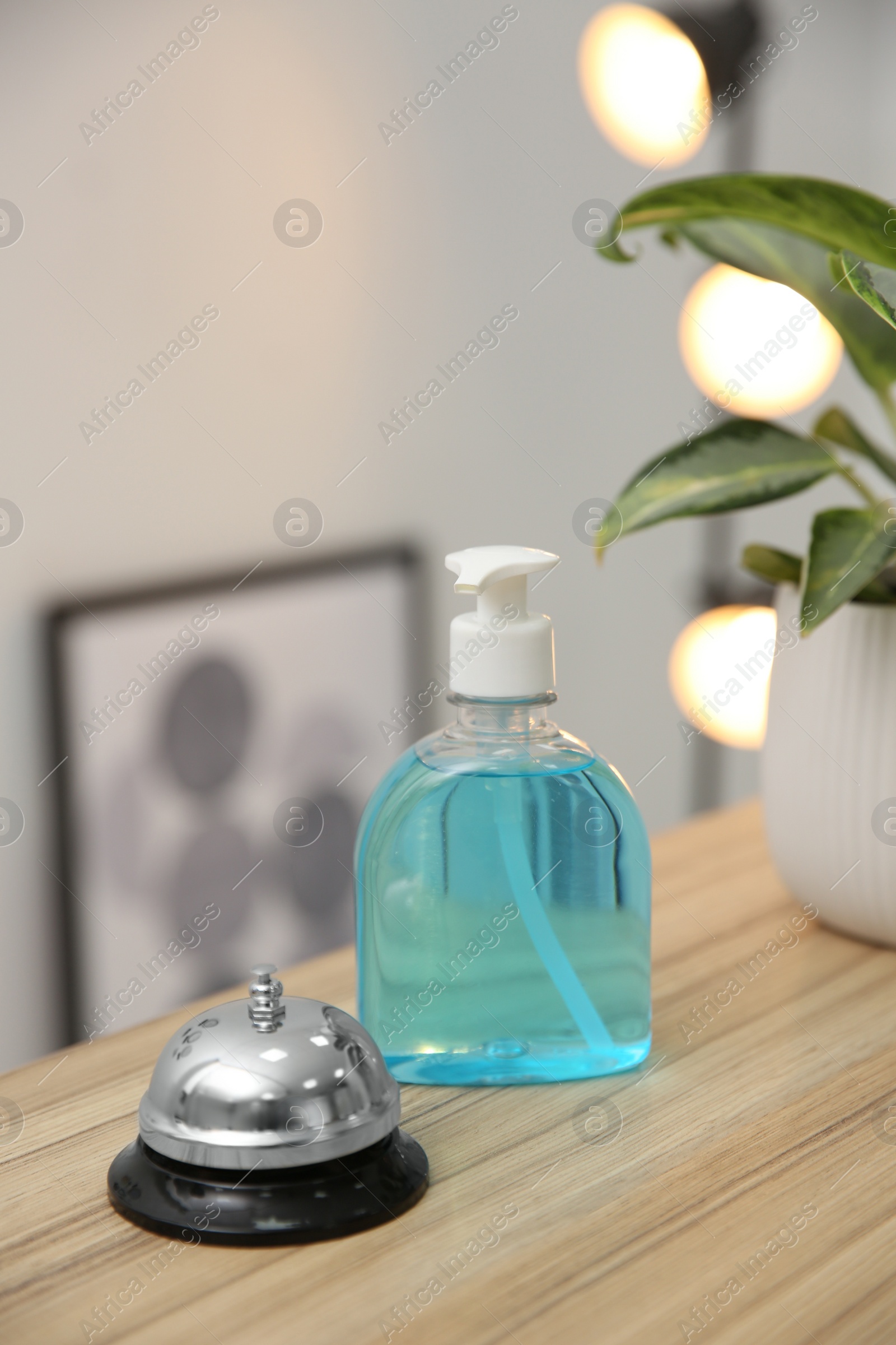 Photo of Dispenser bottle of antiseptic gel and service bell on reception desk in hotel