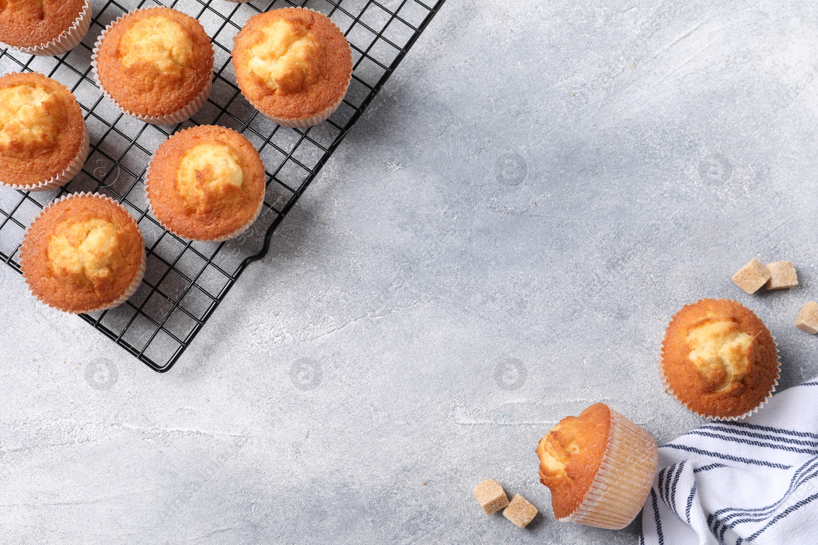 Photo of Delicious sweet muffins and brown sugar on light grey textured table, flat lay. Space for text