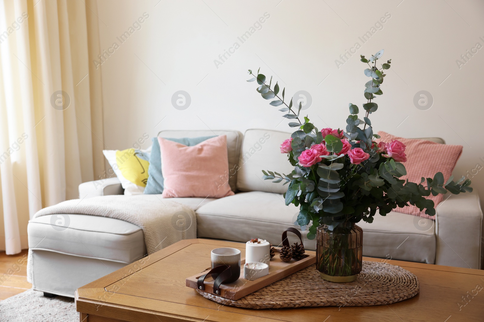 Photo of Beautiful bouquet of roses and eucalyptus branches in vase near candles on table at home. Space for text