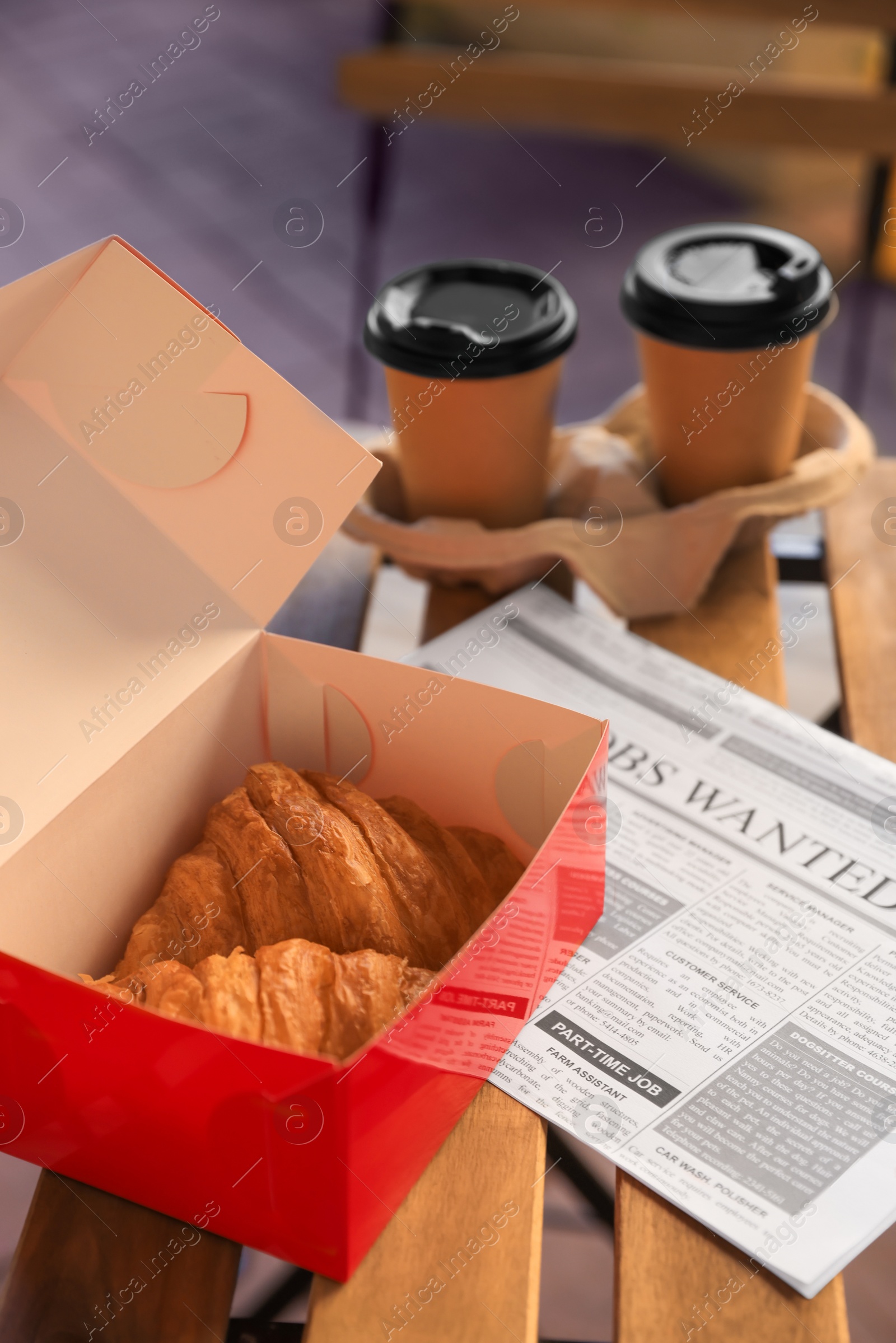 Photo of Tasty croissants, newspaper and cups of coffee on wooden table outdoors