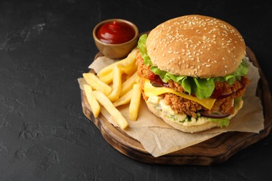 Photo of Delicious burger with crispy chicken patty, french fries and sauce on black table. Space for text