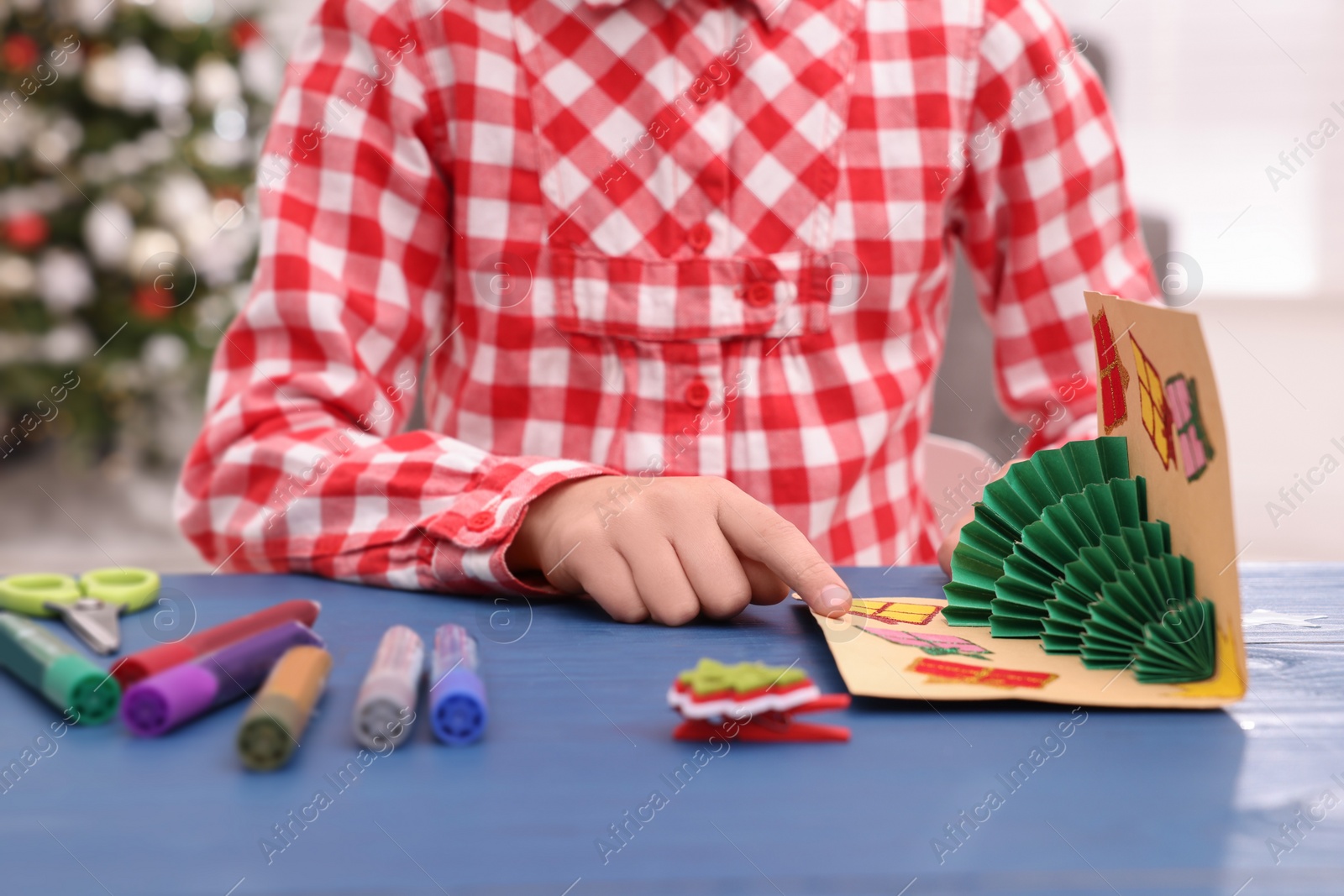 Photo of Little child with beautiful Christmas card at table indoors, closeup