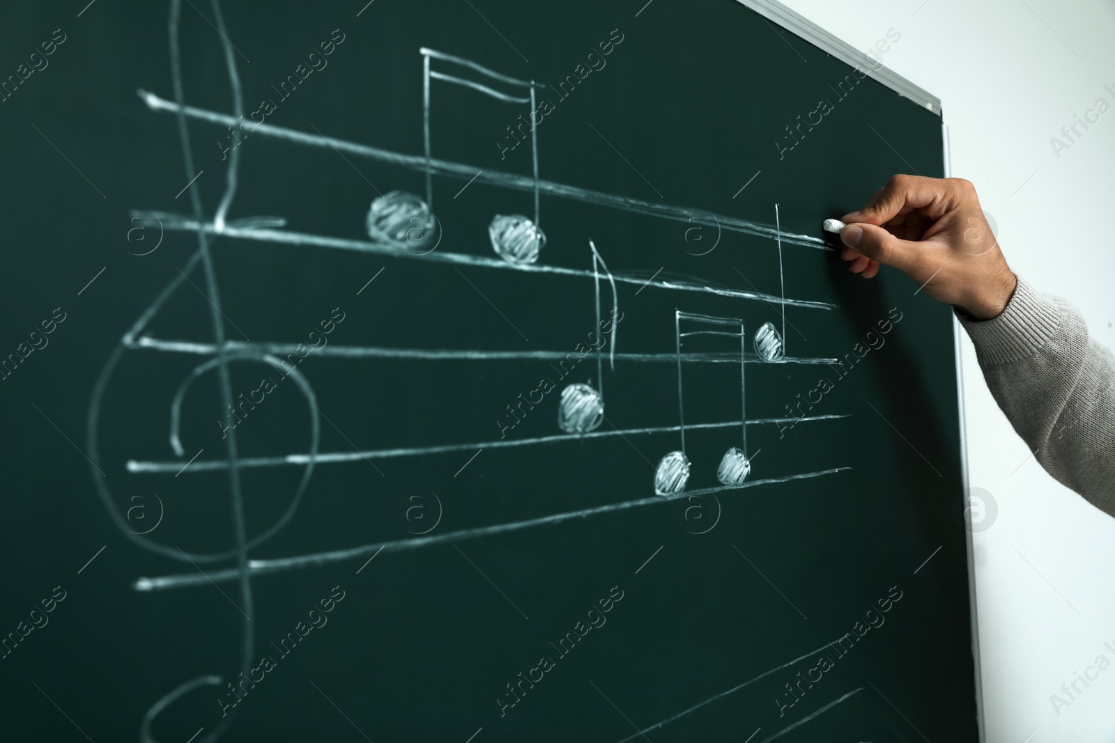 Photo of Teacher writing music notes with chalk on greenboard, closeup