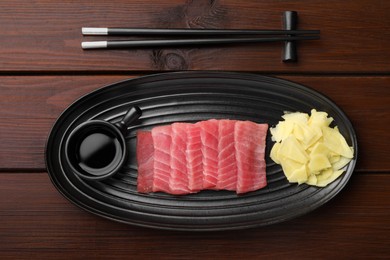 Photo of Tasty sashimi (pieces of fresh raw tuna) served with soy sauce and ginger slices on wooden table, flat lay