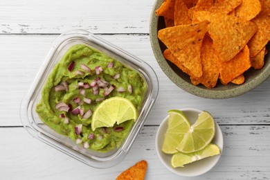 Photo of Bowl of delicious guacamole with onion, lime and nachos chips on white wooden table, flat lay