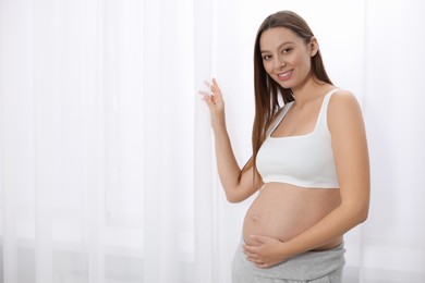 Beautiful pregnant woman near window indoors, space for text