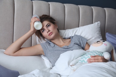 Photo of Exhausted young mother with toy and bottle of milk in bed at home