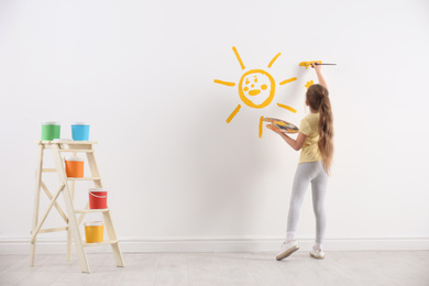 Photo of Little child painting sun on white wall indoors
