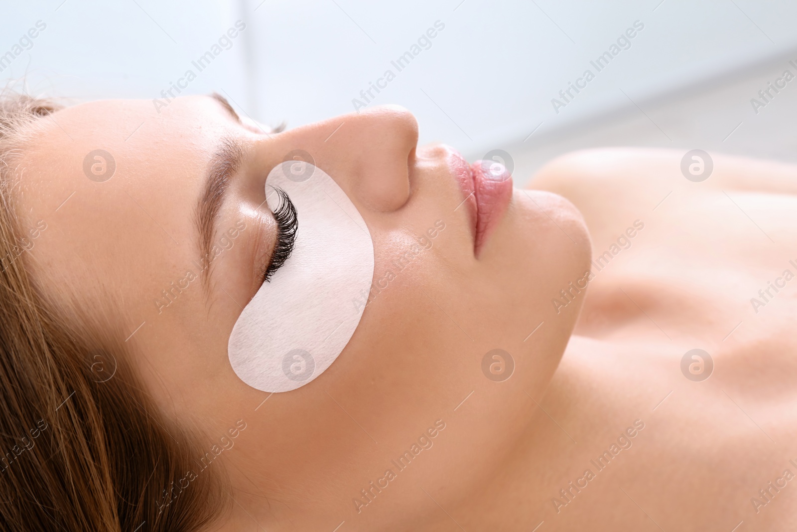 Photo of Young woman undergoing eyelash extensions procedure, closeup