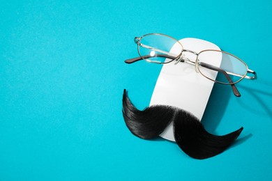 Photo of Artificial moustache, computer mouse and glasses on light blue background, above view. Space for text
