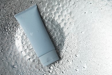 Photo of Moisturizing cream in tube on silver background with water drops, top view. Space for text