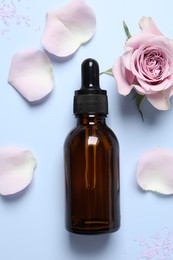 Photo of Bottle of cosmetic serum, flower, petals and sea salt on light blue background, flat lay