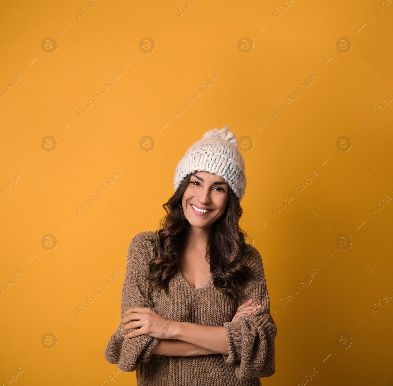 Photo of Young woman in warm sweater and hat on yellow background, space for text. Christmas season