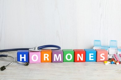 Photo of Word HORMONES made with colorful cubes, stethoscope and pills on white wooden table