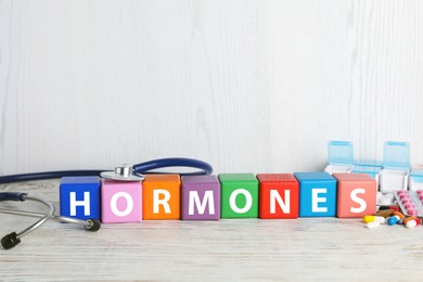 Word HORMONES made with colorful cubes, stethoscope and pills on white wooden table