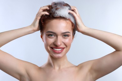 Happy young woman washing her hair with shampoo on light grey background