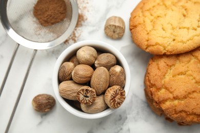 Nutmeg powder, seeds and tasty cookies on white marble table, flat lay