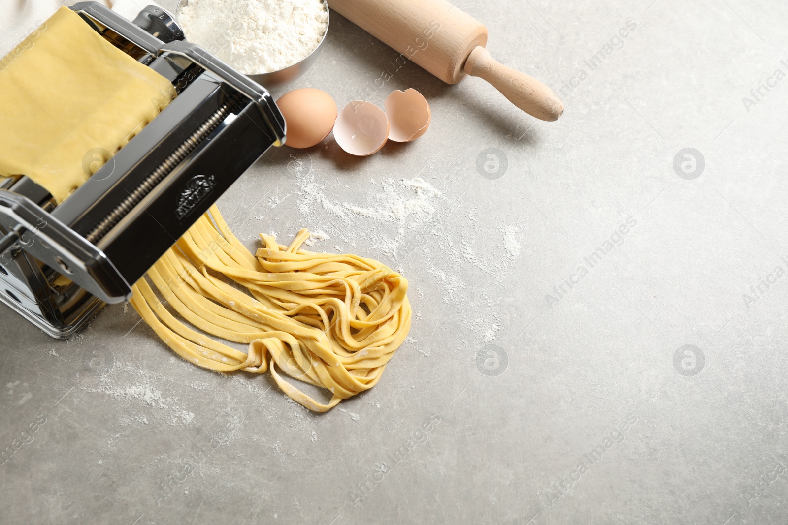 Photo of Pasta maker machine with dough and products on grey table, above view. Space for text