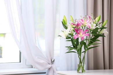 Photo of Vase with bouquet of beautiful lilies on white table indoors. Space for text