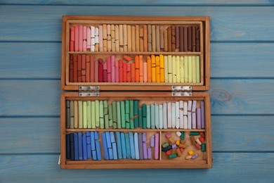 Photo of Drawing pastel set in box on light blue wooden background, top view