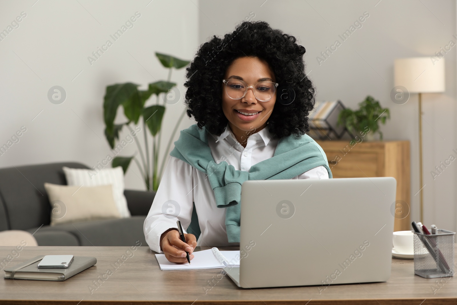 Photo of Happy young woman using laptop at wooden desk indoors