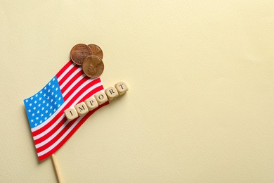 Photo of Word Import made of cubes, coins and small American flag on beige background, top view. Space for text