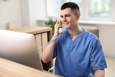 Photo of Smiling medical assistant talking by phone at hospital reception