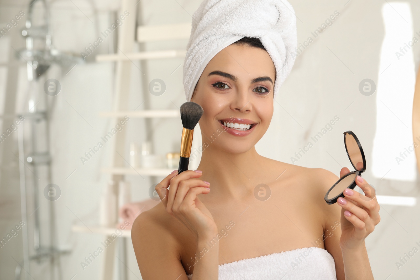 Photo of Beautiful young woman applying face powder with brush in bathroom at home