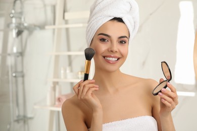 Beautiful young woman applying face powder with brush in bathroom at home