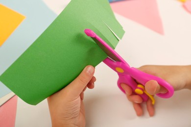 Photo of Little girl cutting color paper with scissors at table, closeup