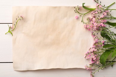 Beautiful Forget-me-not flowers and parchment on white wooden table, flat lay. Space for text