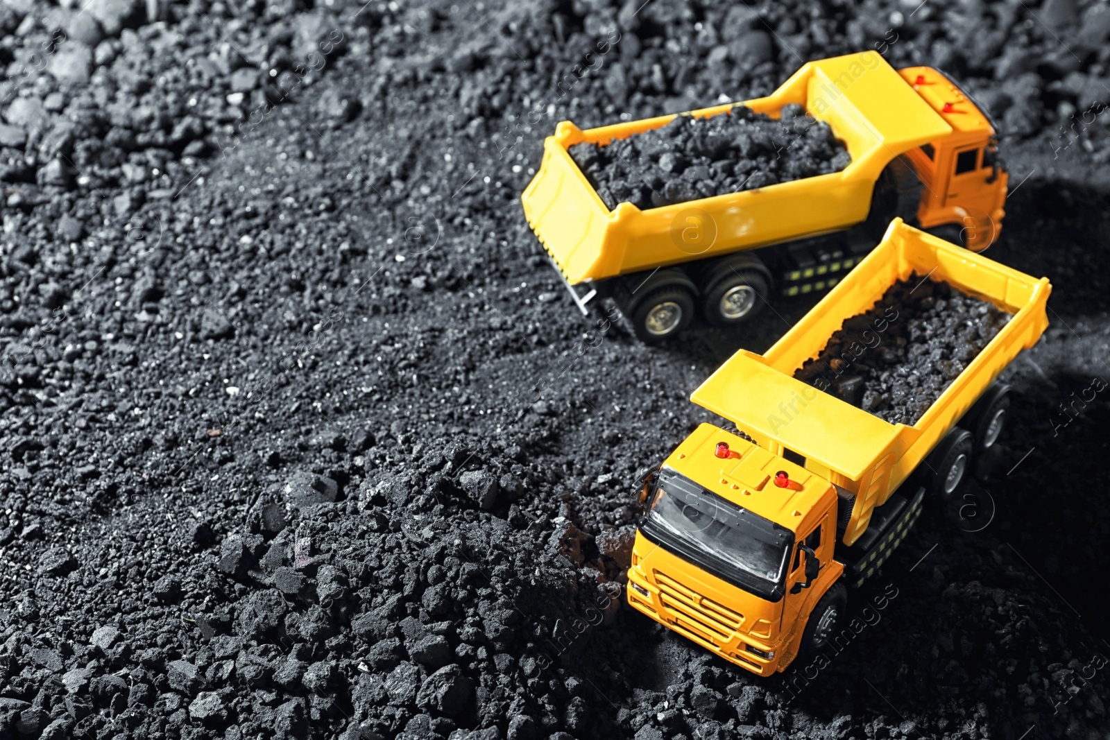 Image of Toy tipper trucks with coal in field. Space for text