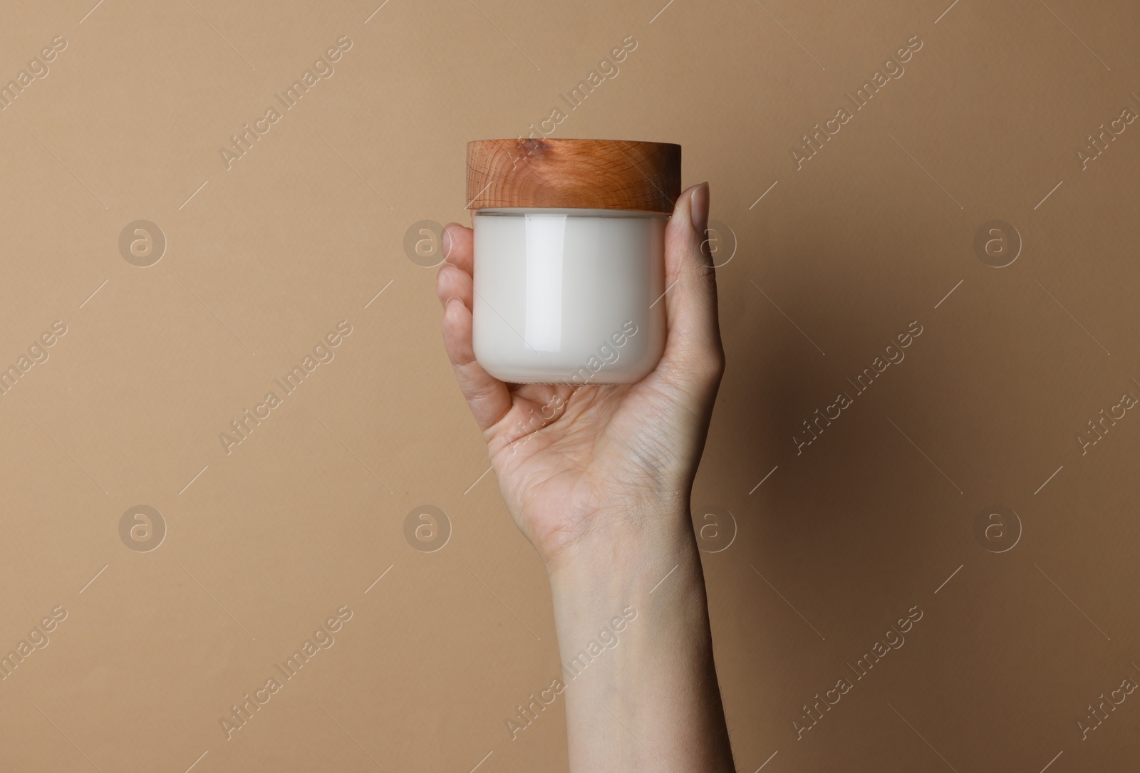 Photo of Woman holding jar of cosmetic product on beige background, closeup
