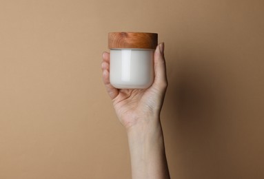 Photo of Woman holding jar of cosmetic product on beige background, closeup