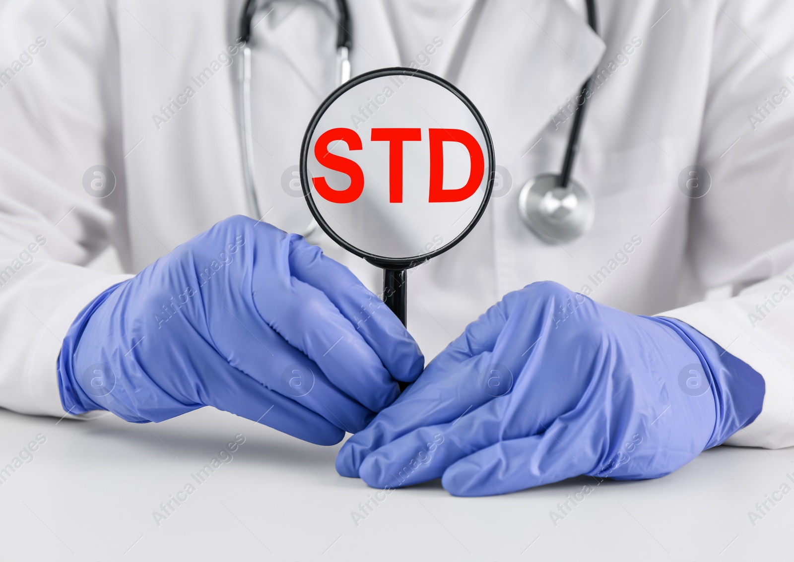 Photo of Doctor holding magnifying glass with abbreviation STD at white table, closeup