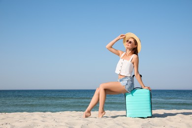 Photo of Beautiful woman with suitcase on sandy beach near sea