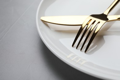 Photo of Plate with golden fork and knife on grey table, closeup. Space for text