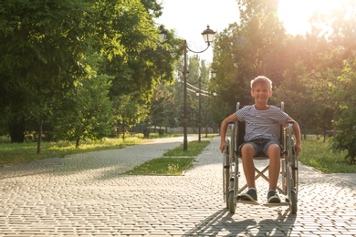 Photo of Happy little boy in wheelchair at park on sunny day. Space for text