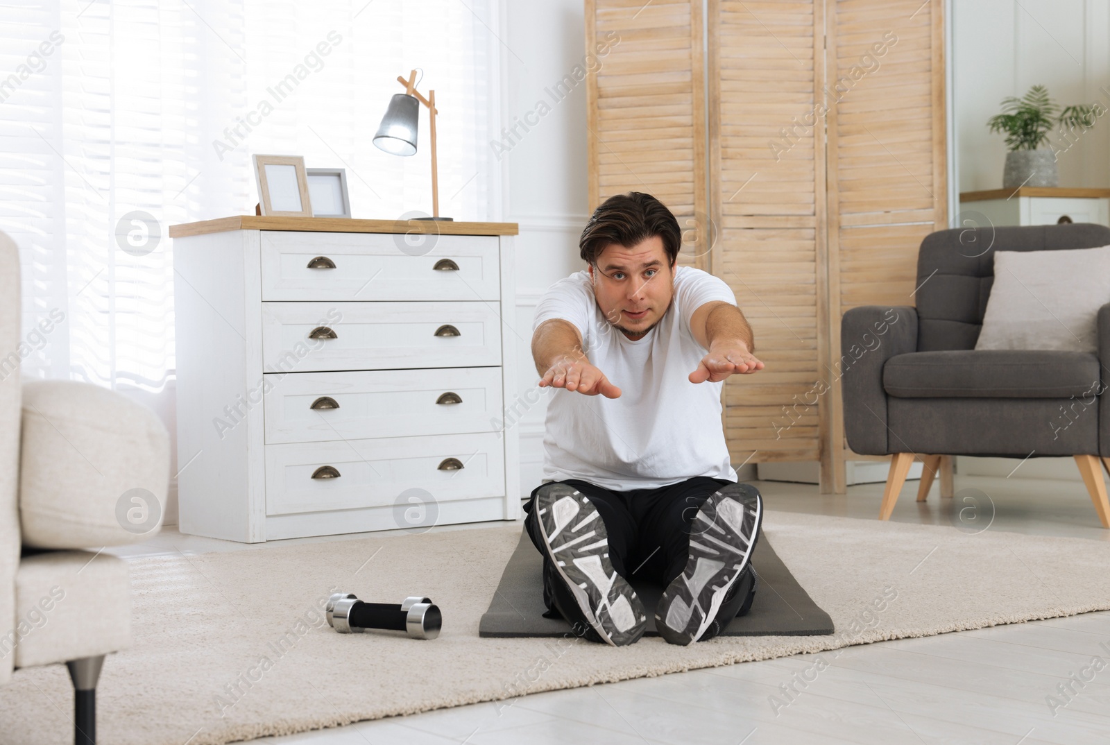 Photo of Overweight man stretching on mat at home, space for text