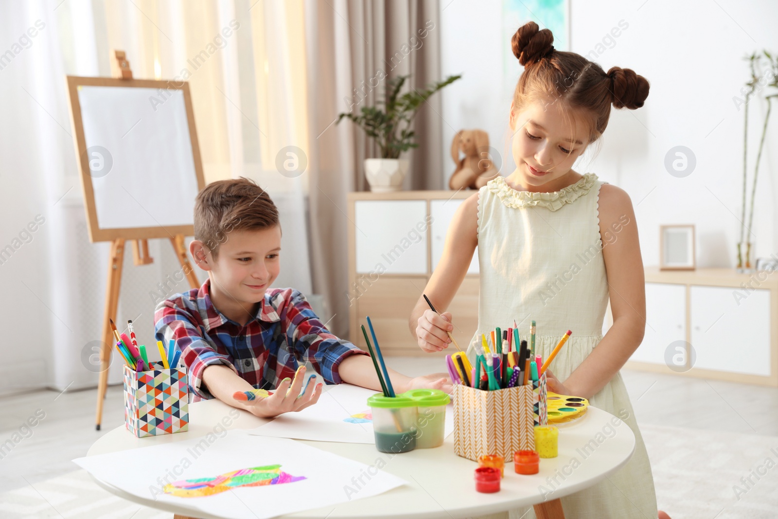 Photo of Little children painting hands at table indoors