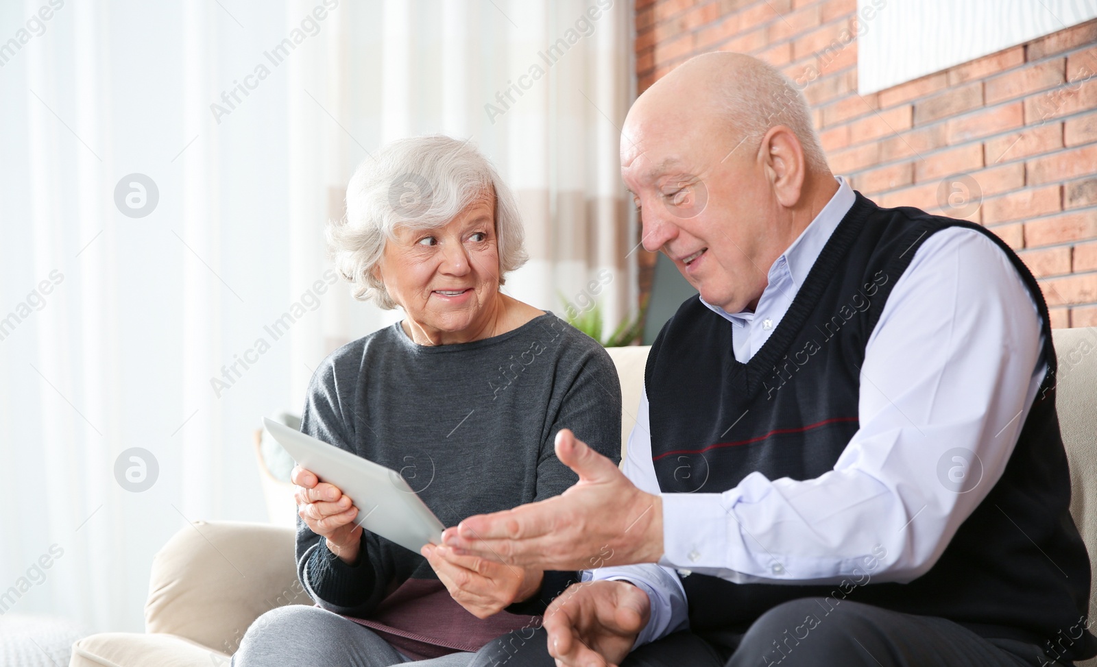 Photo of Elderly couple using tablet PC on sofa in living room