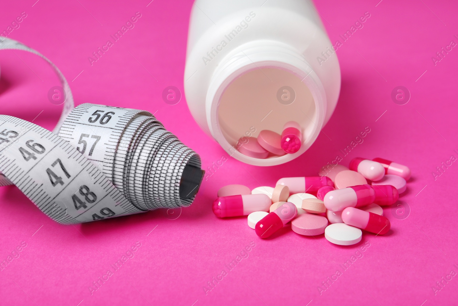 Photo of Weight loss pills, bottle and measuring tape on color background