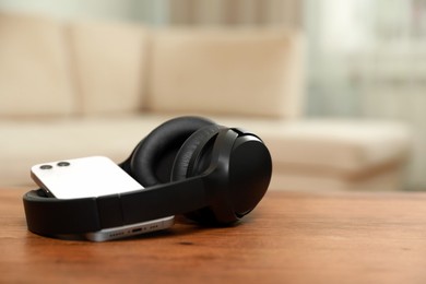 Photo of Modern wireless headphones and smartphone on wooden table indoors, space for text