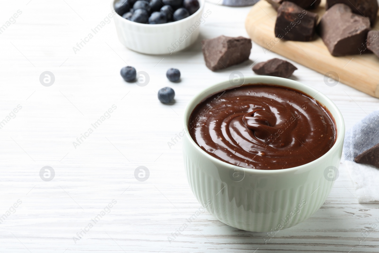 Photo of Delicious chocolate cream and blueberries on white wooden table, space for text